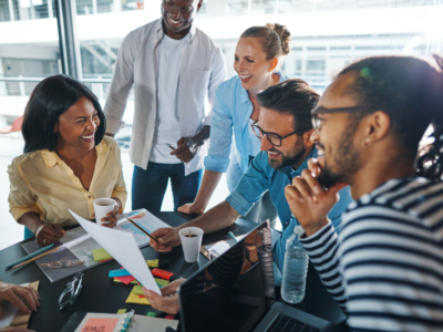 photo of a laughing group of diverse people going over paperwork together in a meeting inside of a glass boardroom in an office