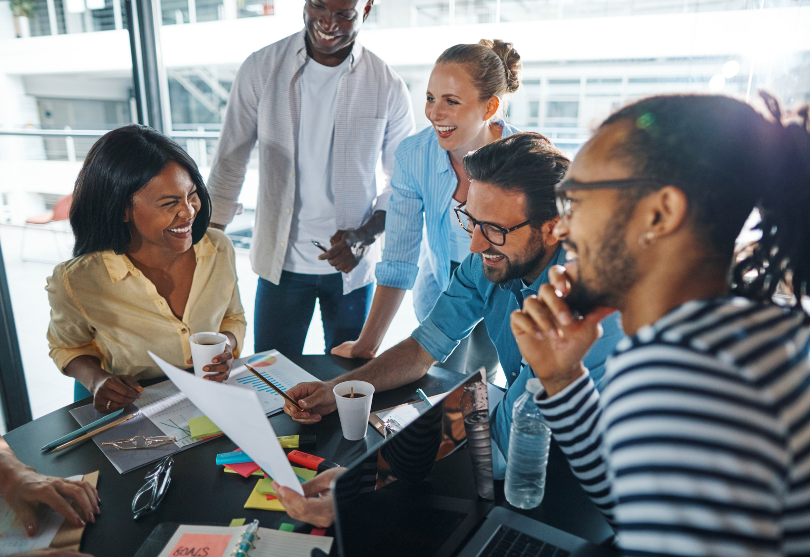 photo of a laughing group of diverse people going over paperwork together in a meeting inside of a glass boardroom in an office