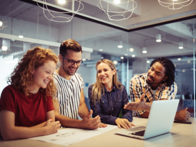 photo of 4 smiling people in an office working on a project on a laptop