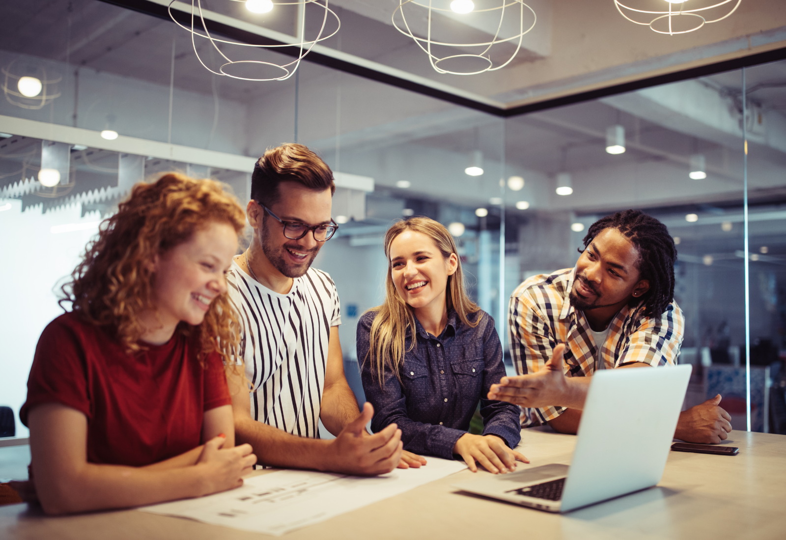 photo of 4 smiling people in an office working on a project on a laptop