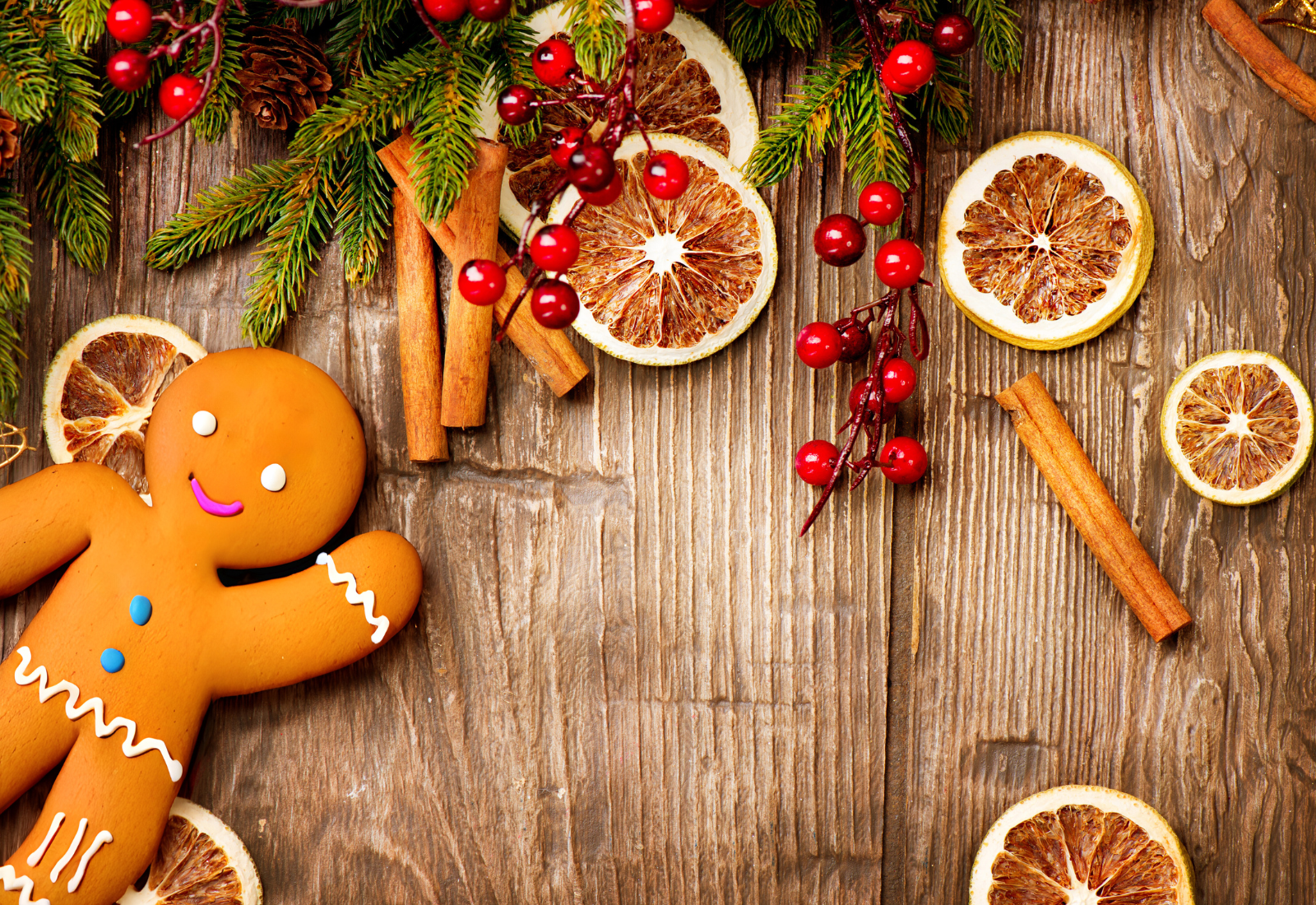 holiday background with fir tree sprigs, red berries, dried orange slices, and a gingerbread man